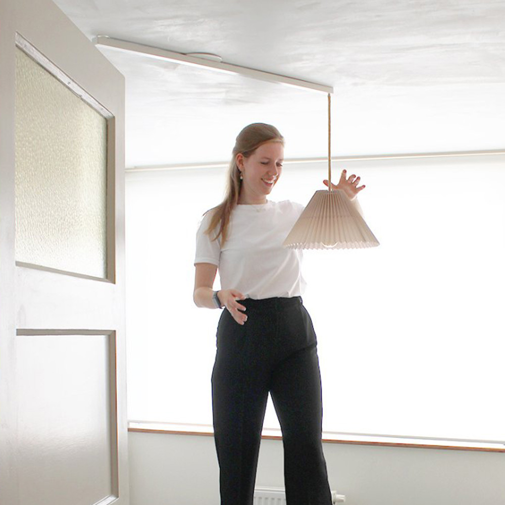 Una mujer cuelga una lámpara colgante en Lightswing Blanco único